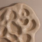 The Organic Treasure Trove Jewelry Dish features a cream-colored ceramic design with wavy edges and multiple oval indents, perfect for displaying your favorite pieces on any beige surface.