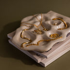 Gold jewelry sits on the Organic Treasure Trove Jewelry Dish, featuring wavy edges, placed on stacked books with a neutral background.