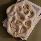 Gold jewelry pieces rest on the Organic Treasure Trove Jewelry Dish, which sits atop stacked papers against a muted backdrop.