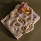 The Organic Treasure Trove Jewelry Dish displays gold jewelry, a pink perfume bottle, and lip gloss on stacked books for a chic minimalist look.