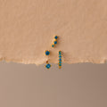 The Blue Zircon Earring Trio Set features three gold earrings with blue zircon stones—a small hoop and an elegant ear climber—displayed on textured beige paper, perfect for a unique birthstone earring set.