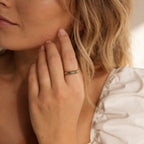 A woman with wavy blonde hair wears a white puff-sleeve top and a gold Half Round Fingerprint Ring on her finger.