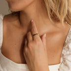 A woman in a white top touches her neck, highlighting the gold Half Round Fingerprint Ring on her finger—a unique and personalized jewelry piece.