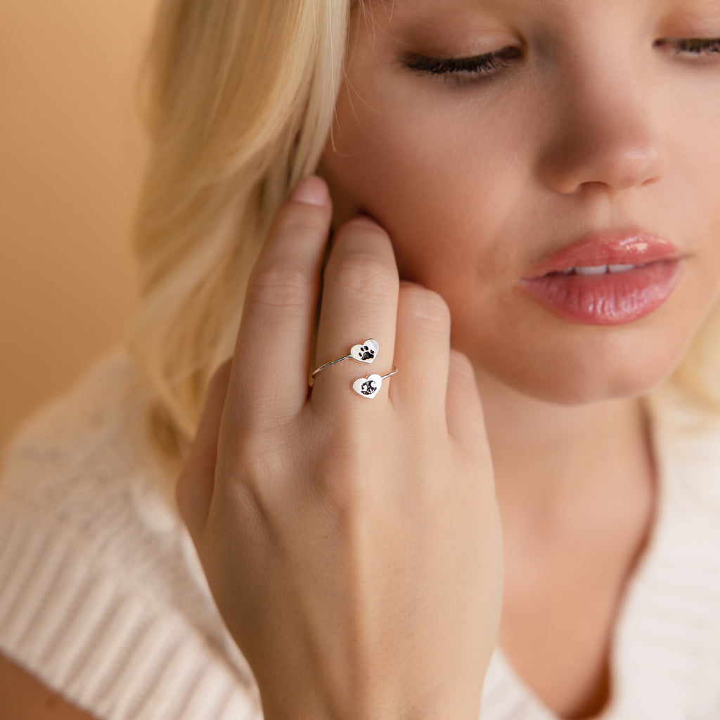 A woman with blonde hair displays the Paw Print Duo Heart Ring, featuring two paw print designs—ideal as a Pet Lovers Gift.