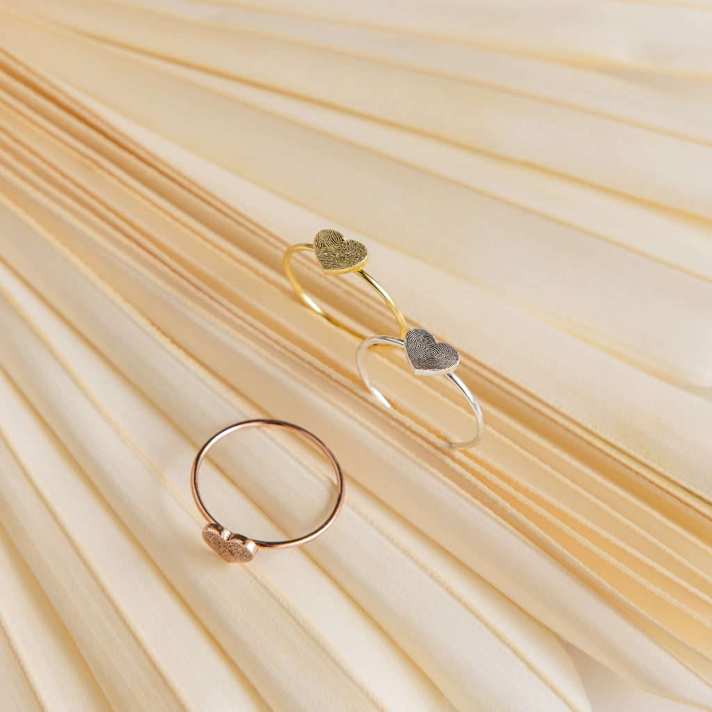The Fingerprint Heart Ring is displayed on soft, cream-colored pleated fabric, highlighting the elegance of personalized jewelry.