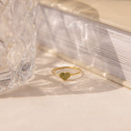 The Fingerprint Heart Ring, crafted in gold, lies on a light surface next to a crystal glass and closed book—a custom piece that captures your unique love and memories.