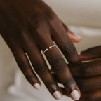A hand wears the Tiny Dual Birthstone Ring—a delicate silver band with two small stones—on the ring finger.