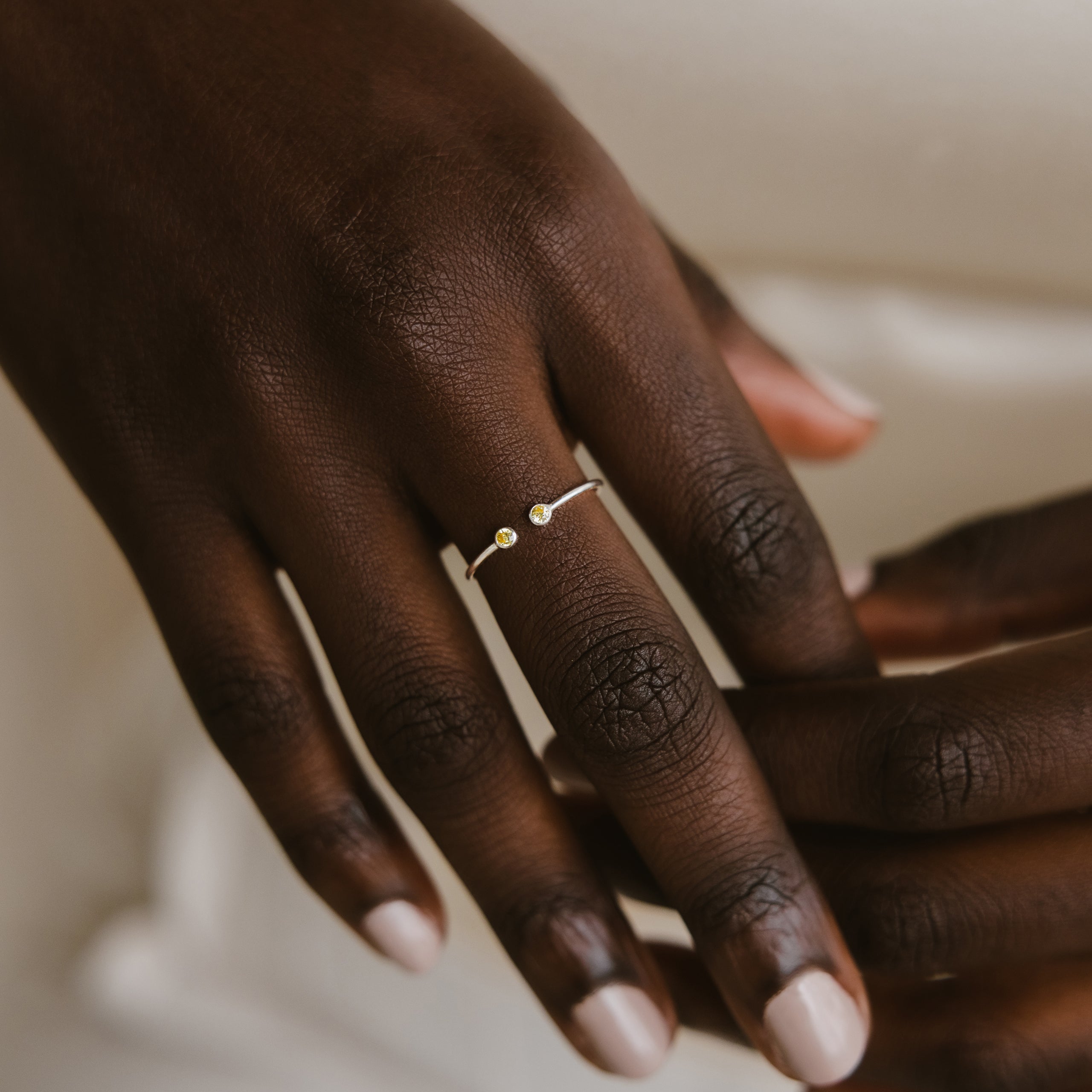 A hand wears the Tiny Dual Birthstone Ring—a delicate silver band with two small stones—on the ring finger.
