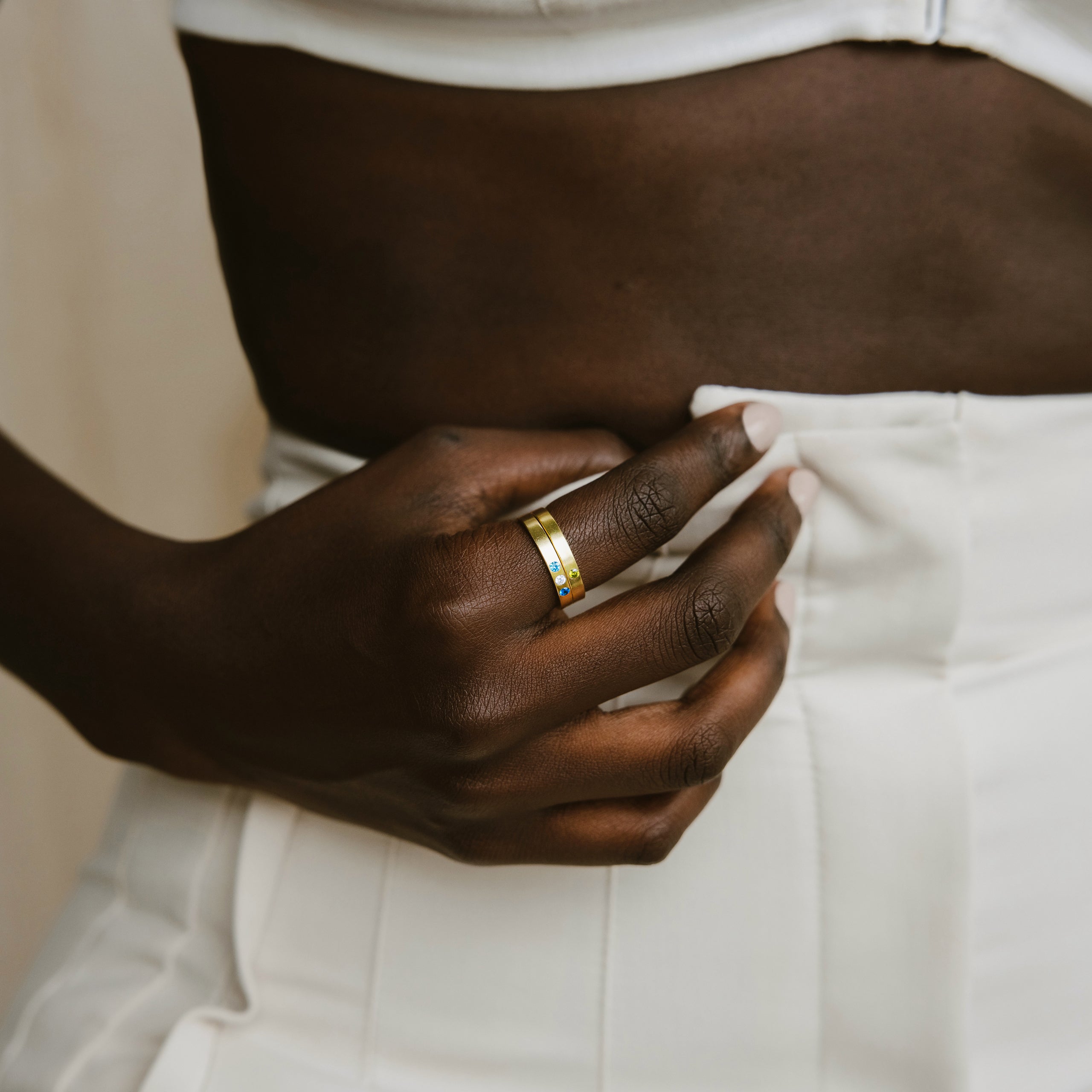 Close-up of a hand wearing the Mothers Birthstone Ring, resting on white high-waisted pants near a bare midriff.