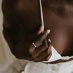 A person wearing the Mothers Birthstone Ring, a silver ring with customizable gemstones, adjusts the strap of a white top, partially revealing their chest and torso.