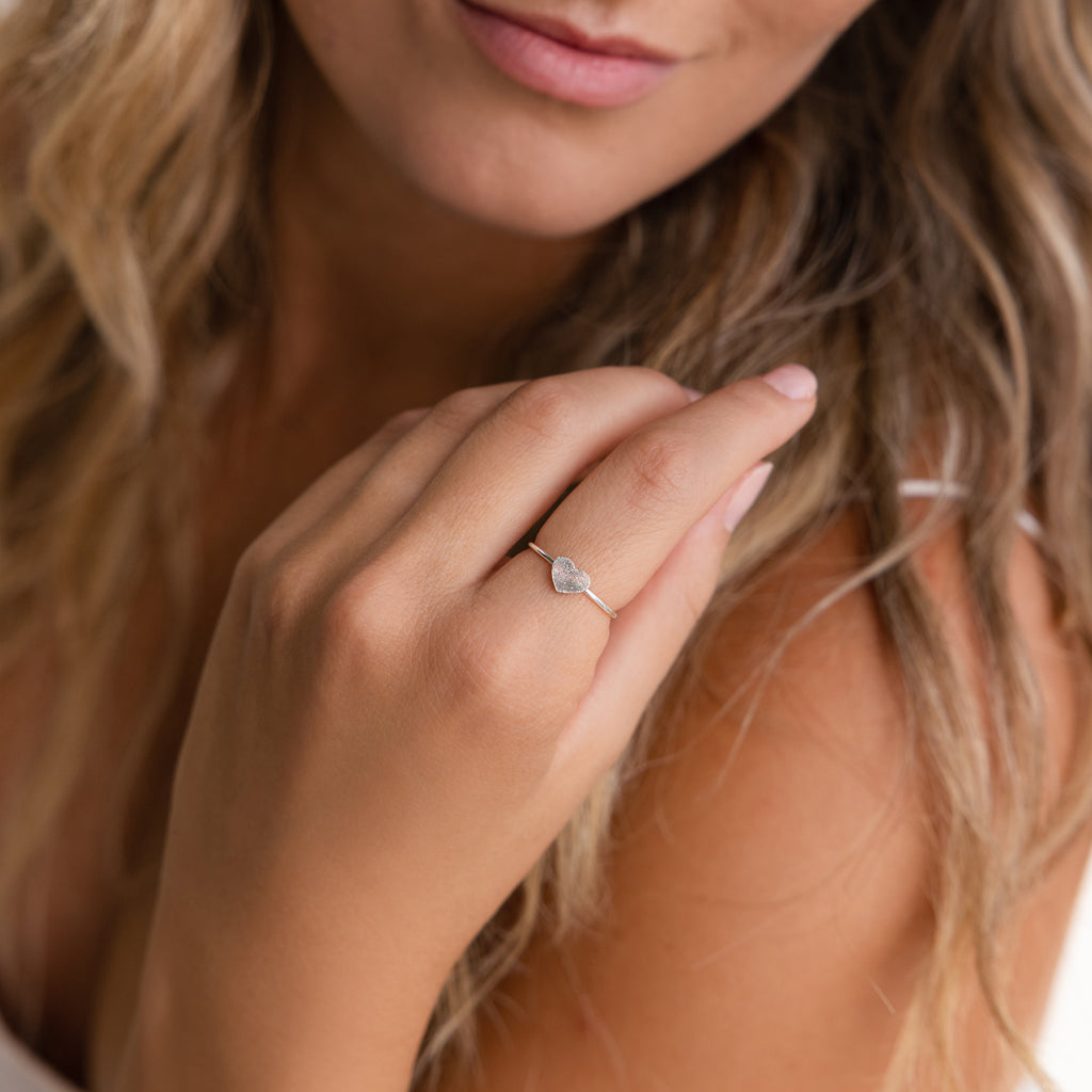 Woman with wavy blonde hair, smiling softly, wears a Fingerprint Heart Ring personalized on her ring finger.