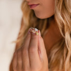 A woman with wavy hair holds the Fingerprint Heart Ring, a customizable piece with three heart-shaped designs in silver, gold, and rose gold.