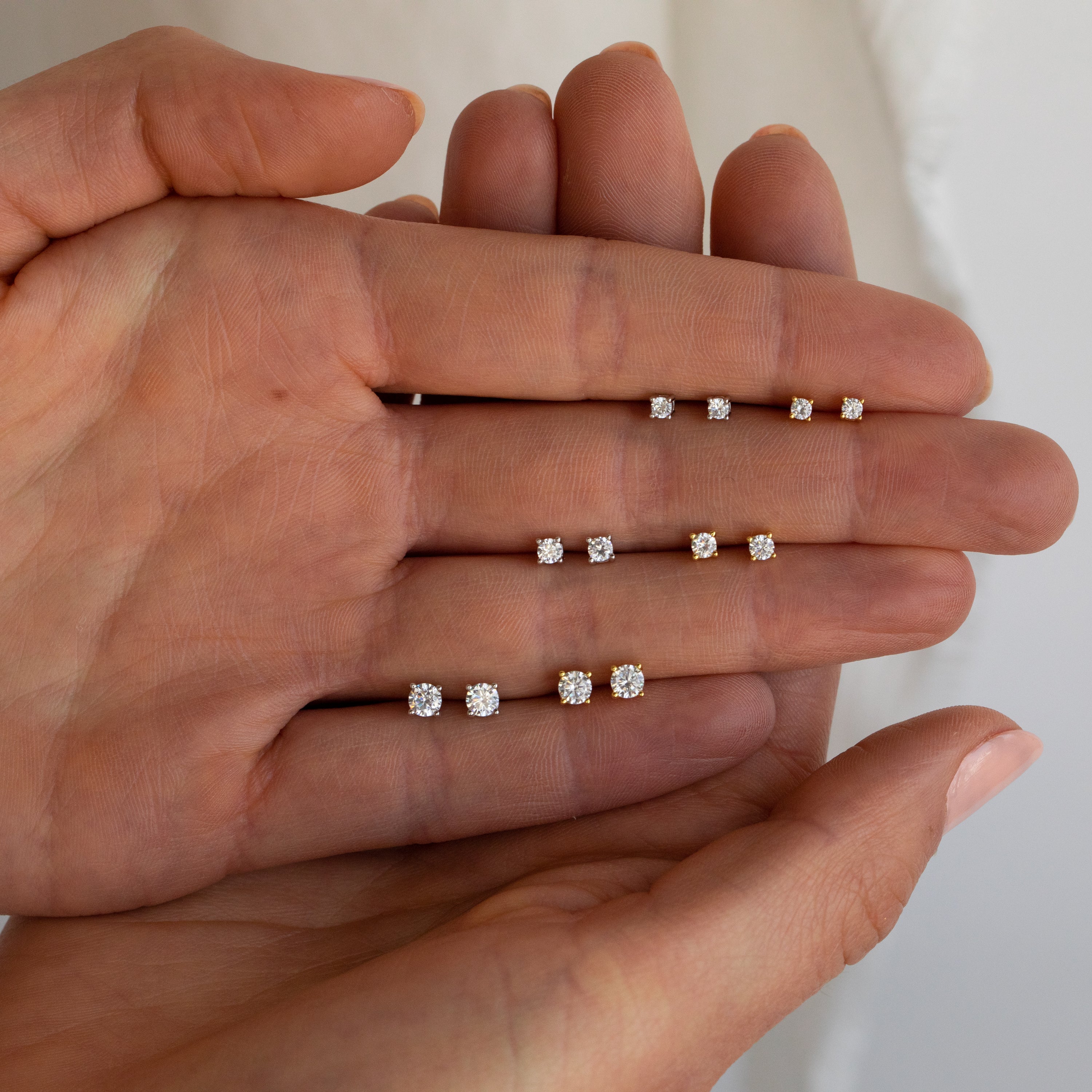 A hand displays the Booker Diamond Studs Set—four pairs of diamond studs in increasing sizes, perfect as lightweight earrings for everyday wear.