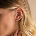 Close-up of a woman's ear with the Booker Diamond Studs Set—four sparkling diamond earrings—nestled among blonde hair tucked behind her ear for an elegant everyday look.