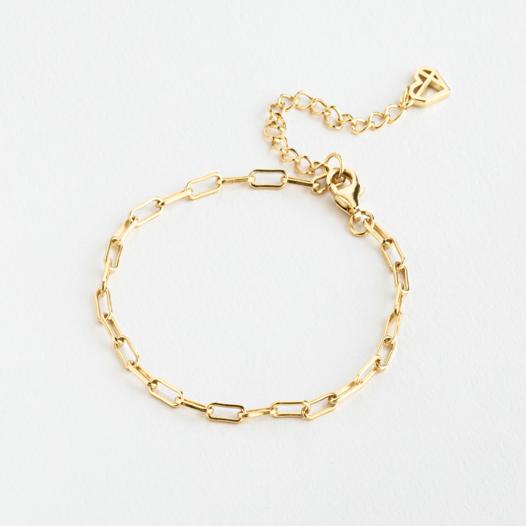 The Essential Bracelet Chains feature a delicate gold chain with rectangular links, an adjustable clasp, and polished geometric style—modern jewelry showcased on a white background.
