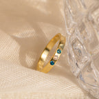 The Mothers Birthstone Ring, featuring two blue stones and one clear stone, rests on beige fabric next to a textured glass for a beautiful personalized keepsake.