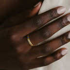 A hand with neatly manicured nails wears the Mothers Birthstone Ring, a gold band engraved with Cancer and set with a small blue gemstone—an ideal personalized keepsake.