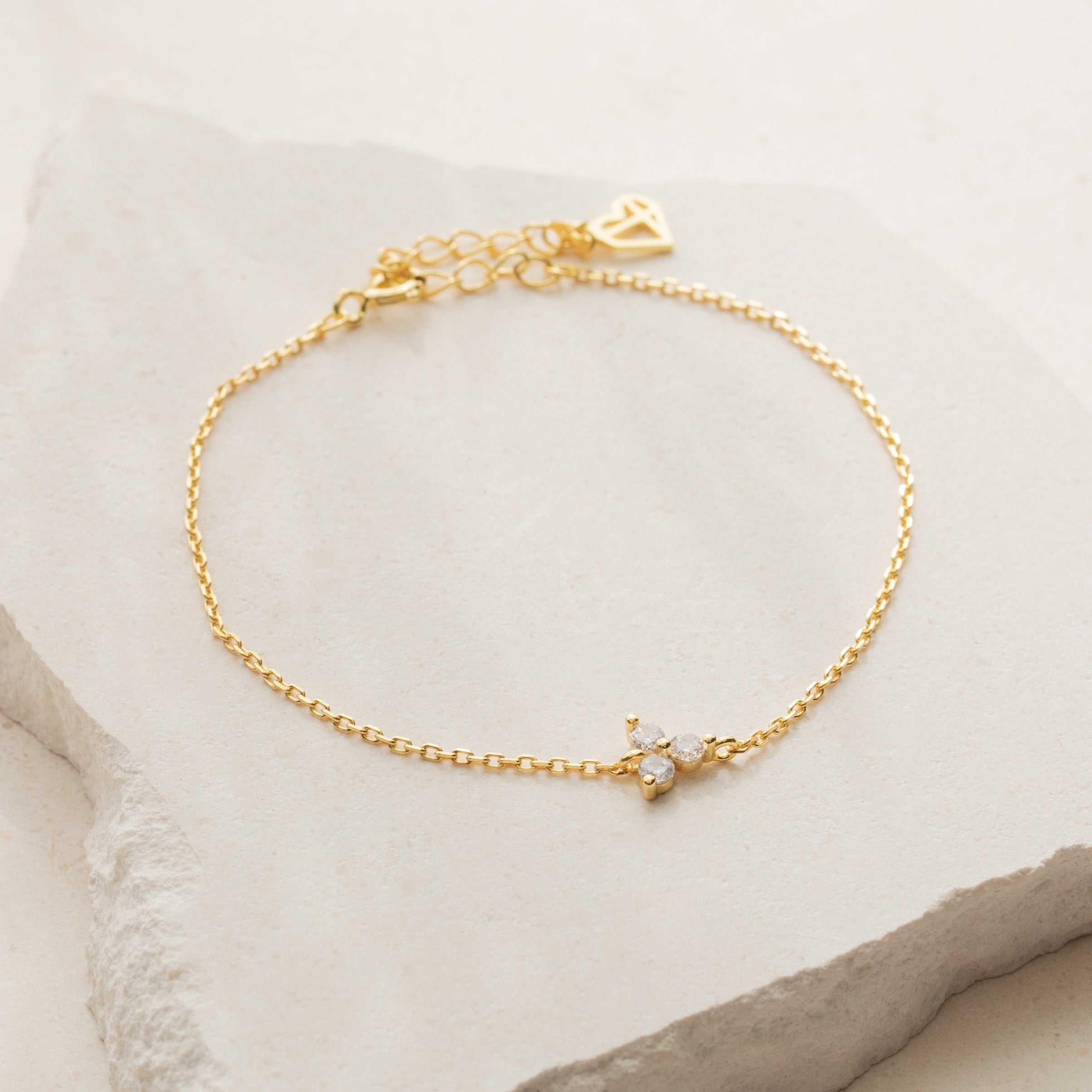 The Lily Diamond Bracelet features a delicate gold chain with a butterfly-shaped pendant and adjustable clasp, perfect for evening wear. Displayed elegantly on a stone surface.