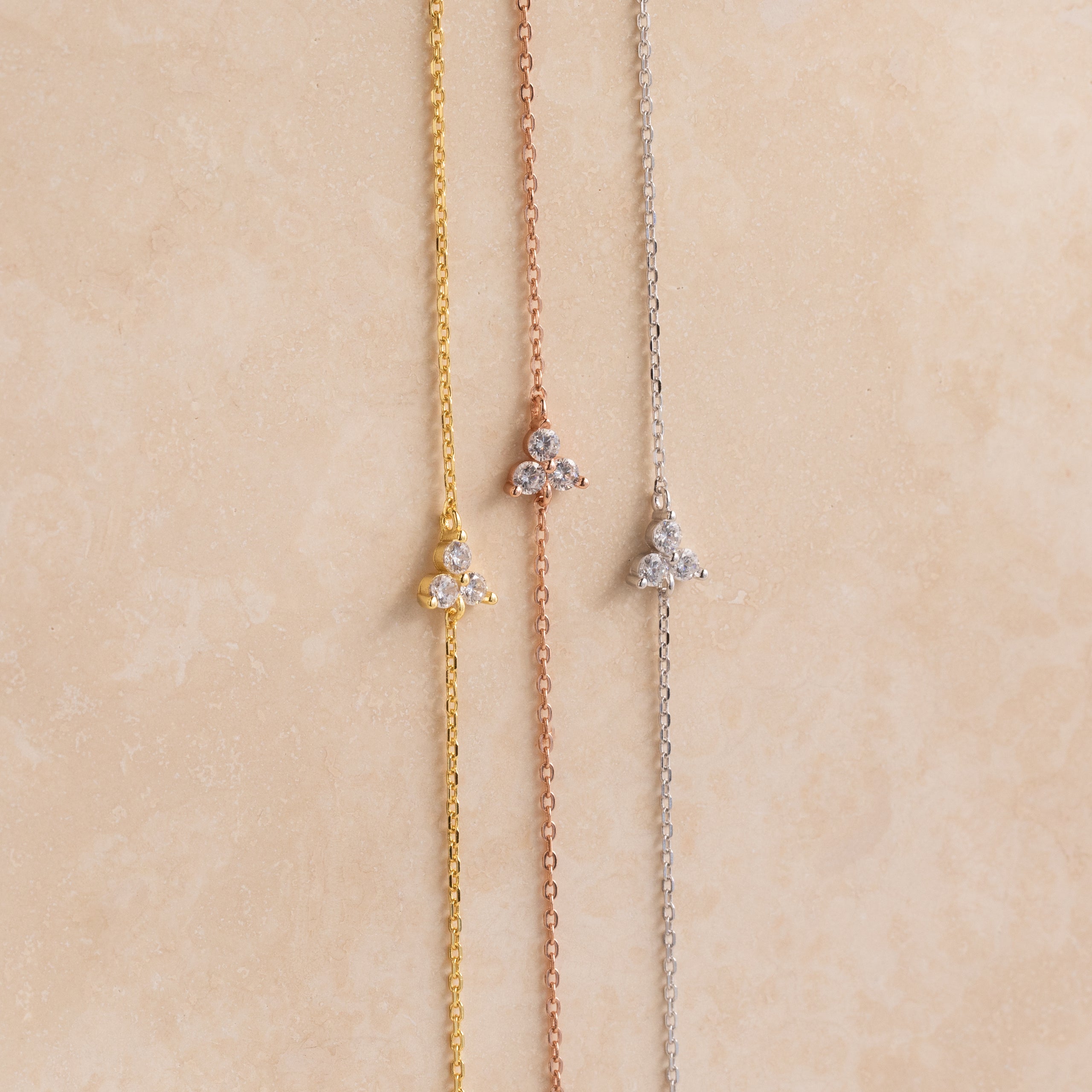 The Lily Diamond Bracelet features three delicate chains in gold, rose gold, and silver, each adorned with a small three-stone diamond cluster—perfect for adding subtle sparkle to your evening attire.