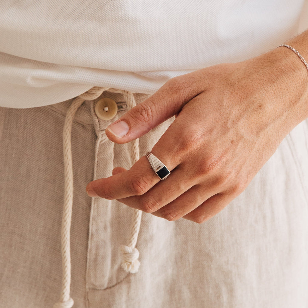 A hand wearing the Black Signet Ring, paired with a white shirt and beige drawstring pants.