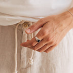 A hand wearing the Black Signet Ring, paired with a white shirt and beige drawstring pants.