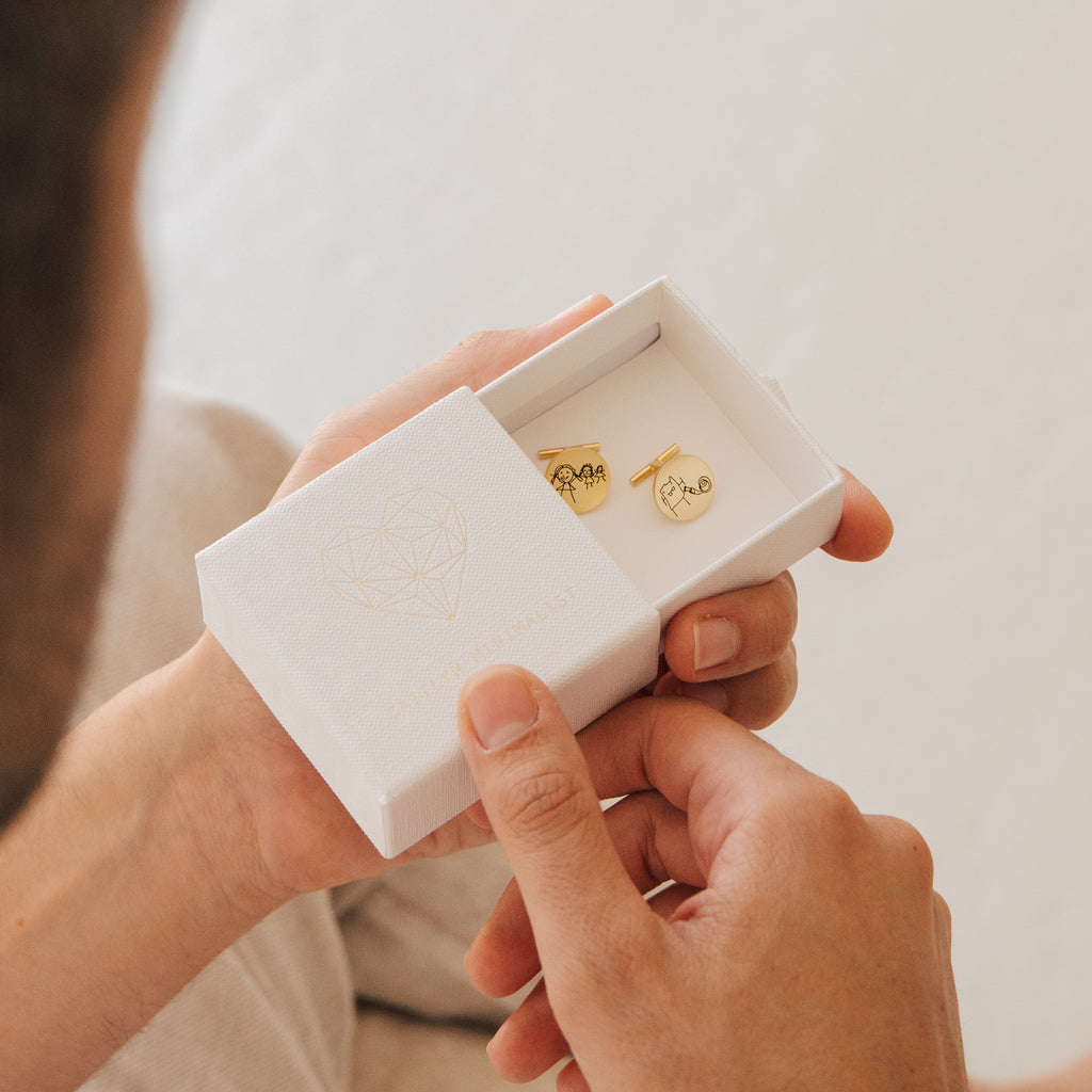 A person holds an open white box containing two Engraved Cufflinks.