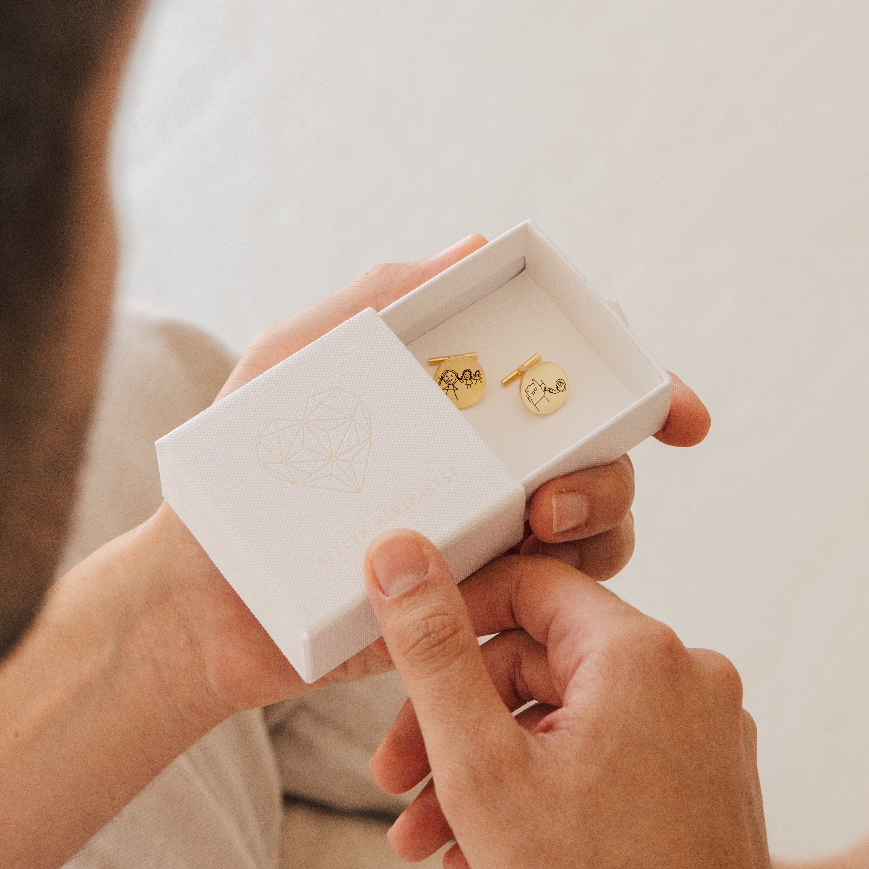 A person holds an open white box containing two Engraved Cufflinks.