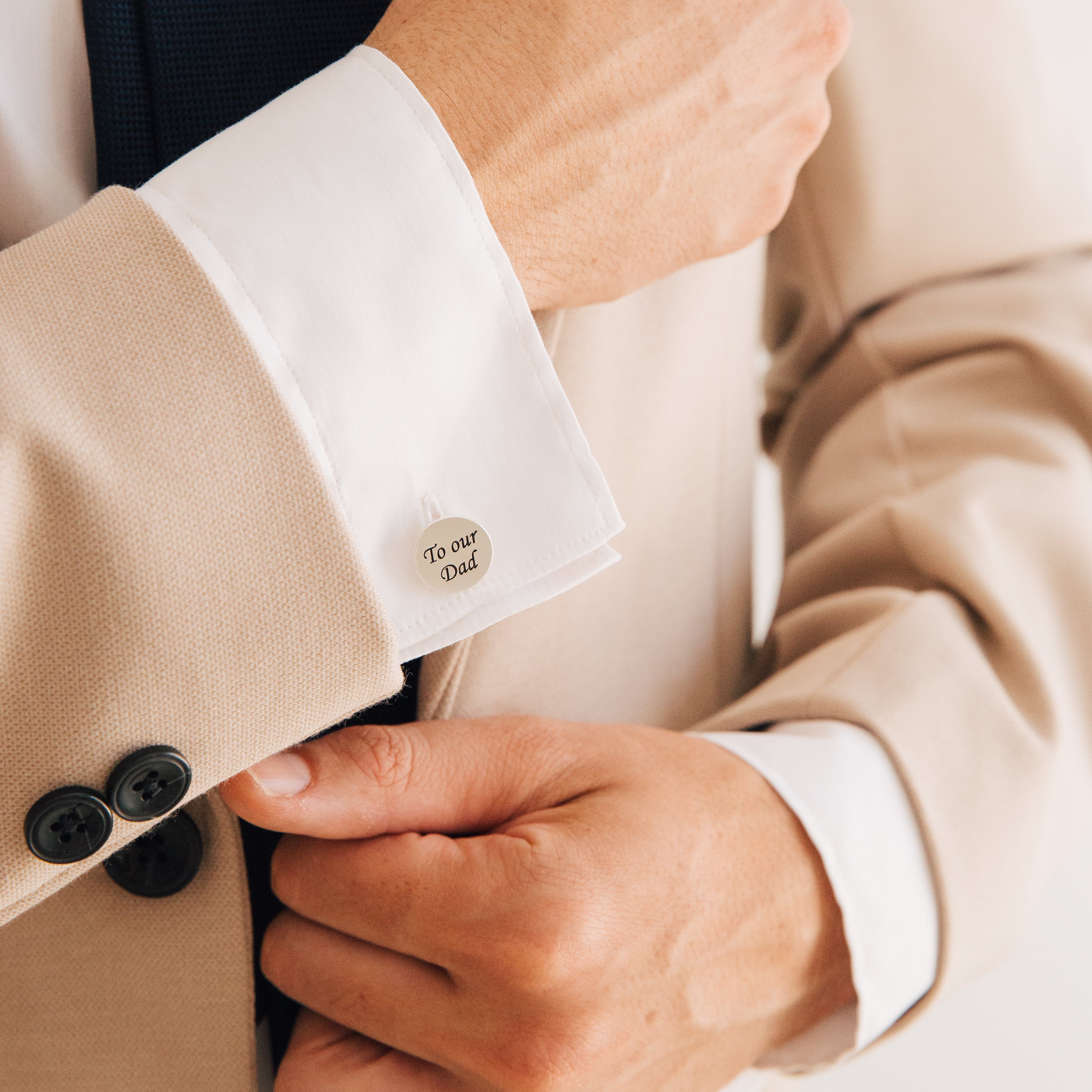 A person in a beige suit adjusts their cuff, revealing Engraved Cufflinks personalized with "To our Dad.
