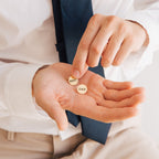 A man in a tie holds two round pins reading BEST and DAD, resembling the Engraved Cufflinks—an ideal personalized gift for celebrating fatherhood.