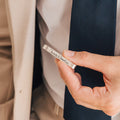 A man in a suit holds a silver Handwriting Tie Clip engraved with "Charlotte & Amadéo," making it an ideal personalized gift.