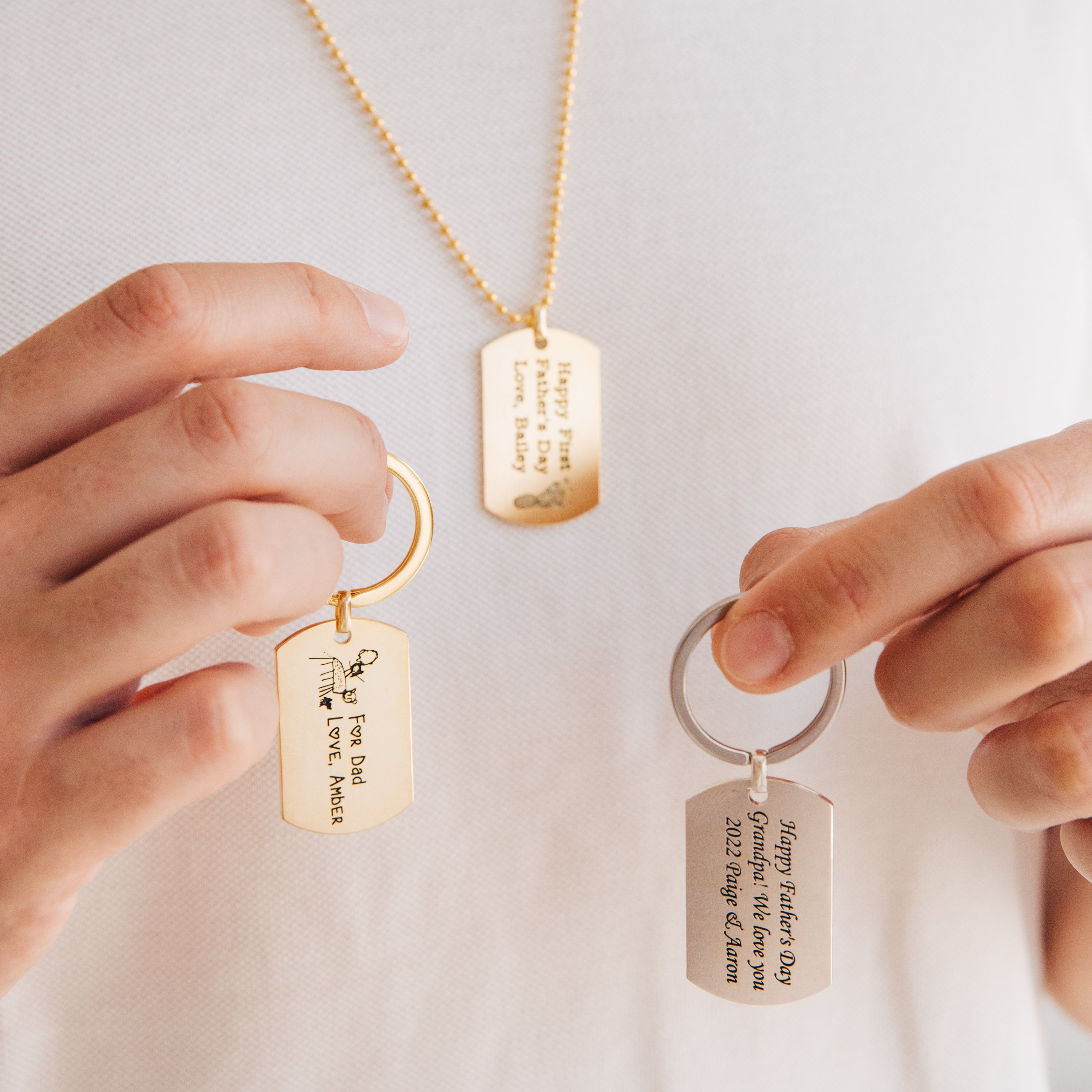 A person holds three engraved Handwriting Dog Tag Keychains with personalized messages—an ideal Father's Day gift for a truly unique touch.