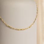 The Mini Name Bar Necklace showcases a gold chain with three custom name tags—Piper, Adam, and Charlotte—set against a neutral background.