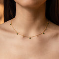 A woman wears the Larissa Emerald Station Necklace—a delicate gold chain featuring dainty green and clear gemstone charms in a vintage-inspired design.