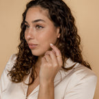 Woman with curly brown hair in a cream blouse looks to the side, gently touching her face with a hand adorned by the Layla Opal Diamond Ring.