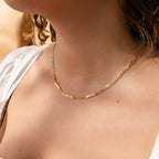 A woman wearing the Mini Name Bar Necklace in gold with a white top, shown from the shoulders to the chin.