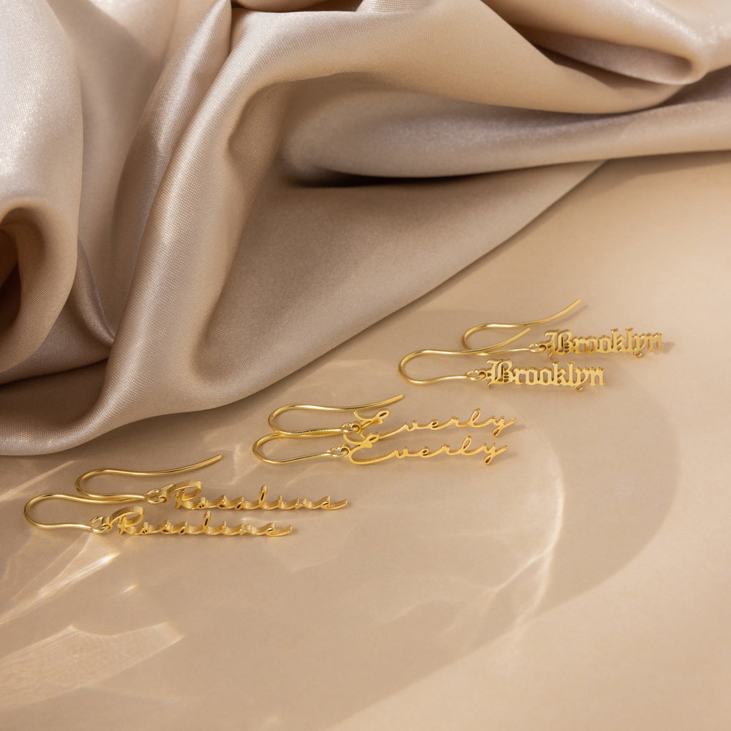Three Old English Dangling Name Earrings reading Brooklyn and Everly rest on beige satin—perfect as custom, handmade drop earrings or a personalized gift for someone special.