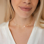 A woman smiles softly in a white blouse, wearing the Apollo Letter Name Necklace featuring minimalist lettering that spells EVERLY.