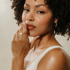 Woman with curly hair in a white top, touching her chin and lips as she looks at the camera—inspiration for a personalized Pet Signet Ring.