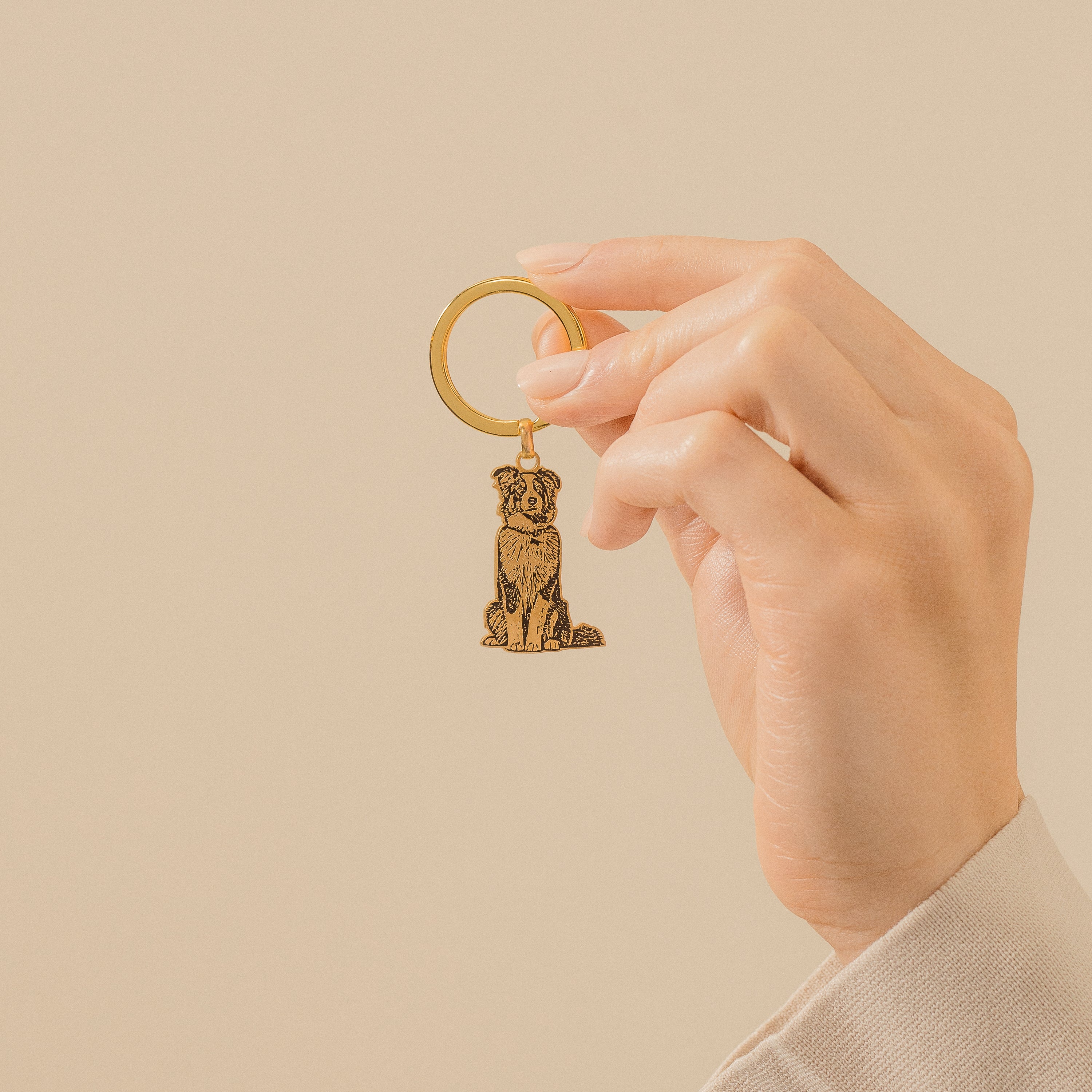 A hand holds a gold Custom Pet Keychain with a dog-shaped charm against a beige background.