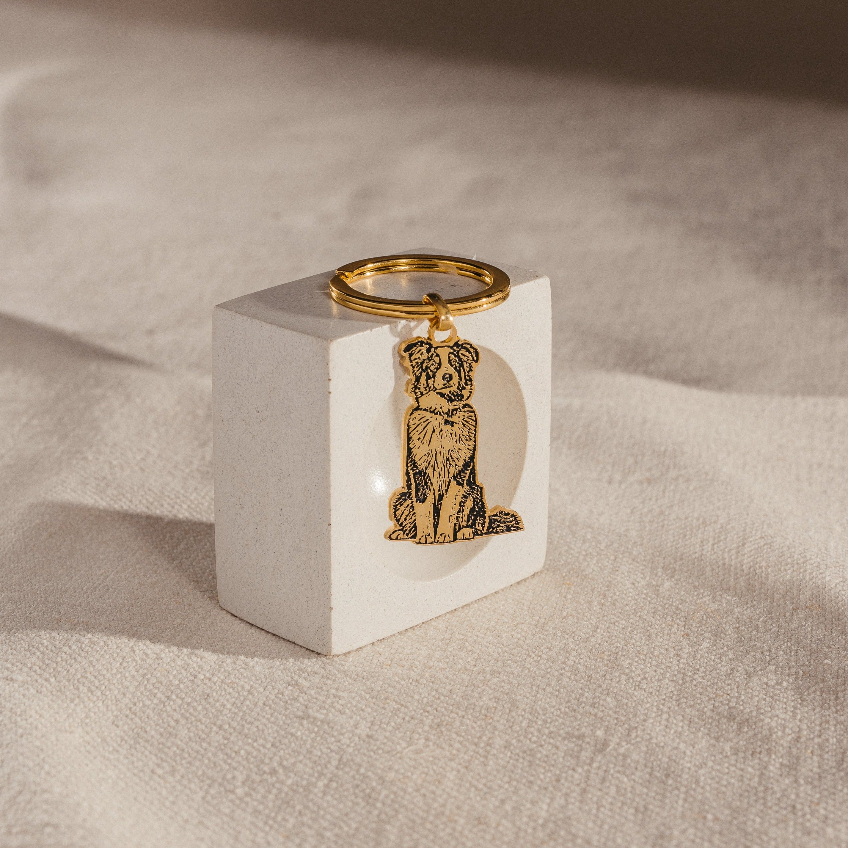 Custom Pet Keychain featuring a dog engraving, shown on a white rectangular block over beige fabric—a personalized keepsake to celebrate your furry friend.