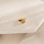 The Pet Signet Ring, engraved with a cat face, sits on a cream geometric surface—an adorable and personalized piece of pet jewelry.