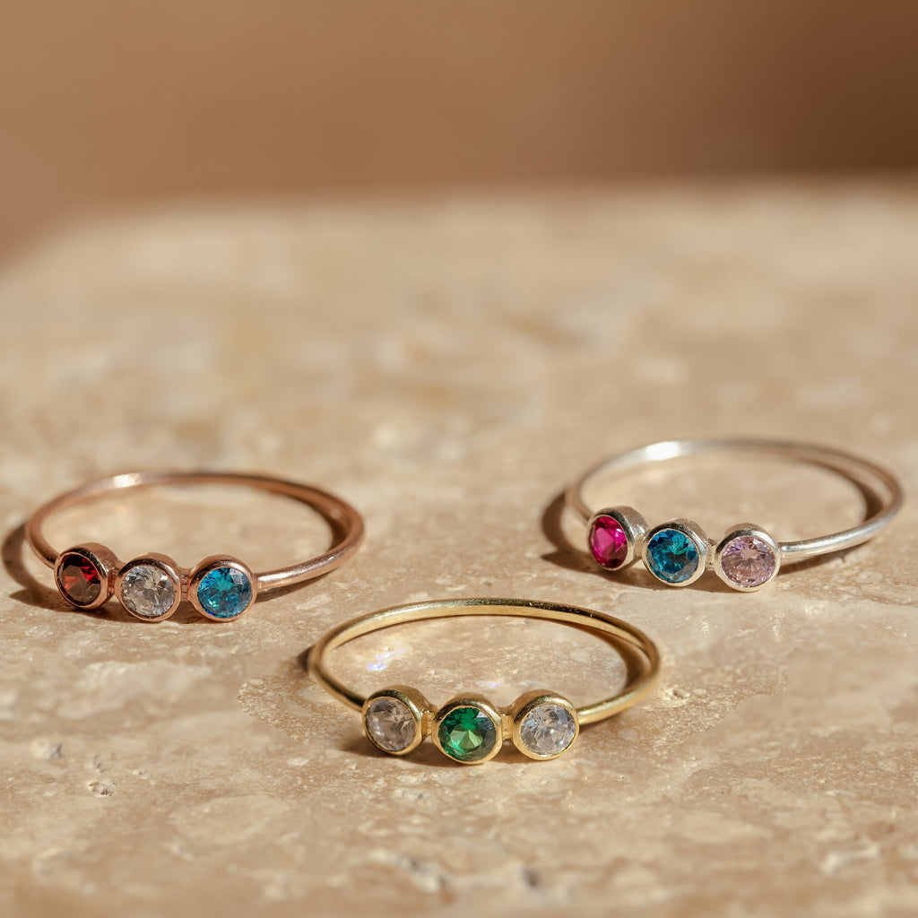 The Triple Birthstone Ring is a customizable ring featuring three bands, each set with a different colored stone.