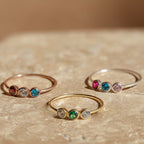 The Triple Birthstone Ring is a customizable ring featuring three bands, each set with a different colored stone.