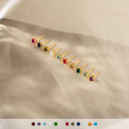 Twelve Booker Large Birthstone Studs with vibrant gemstones are arranged in a row on soft beige fabric—perfect as a personalized earrings jewelry gift.