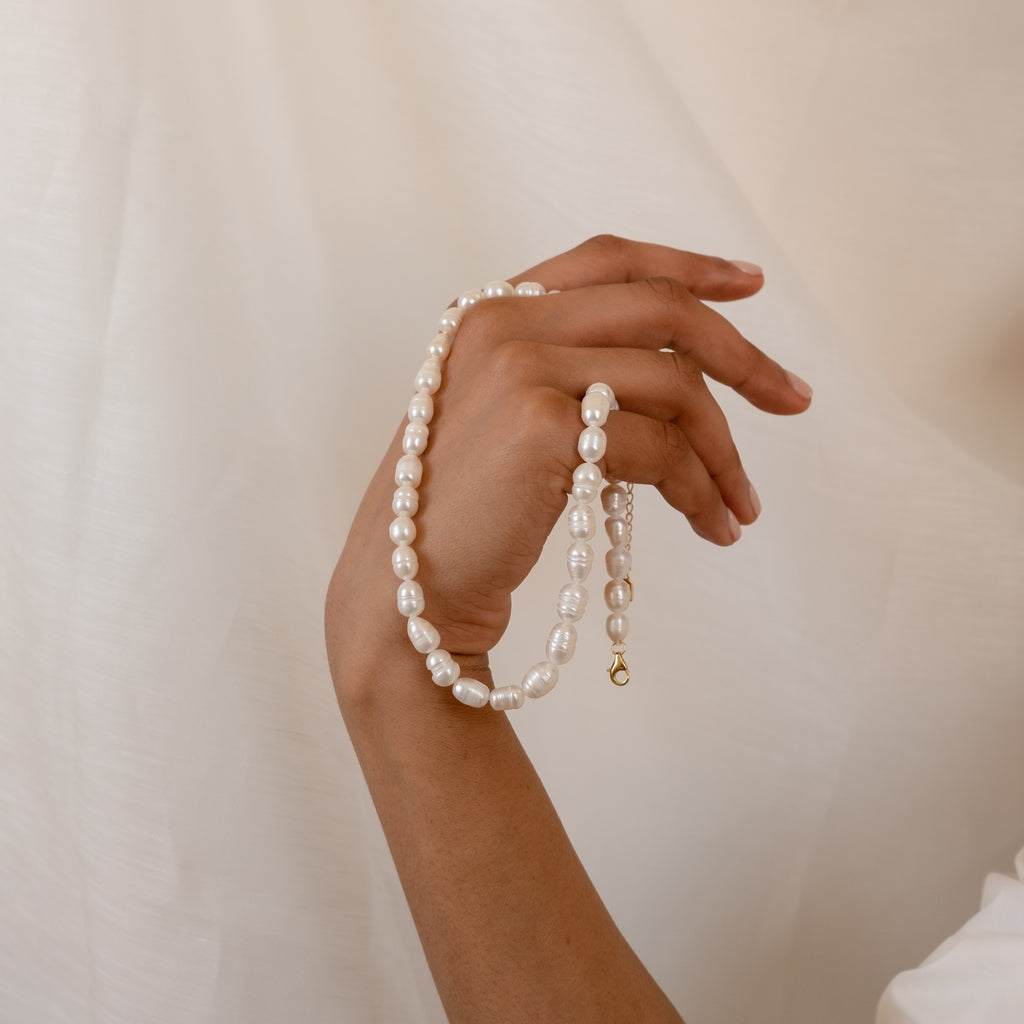 A hand elegantly displays the Bold Pearl Necklace against a soft, light background.