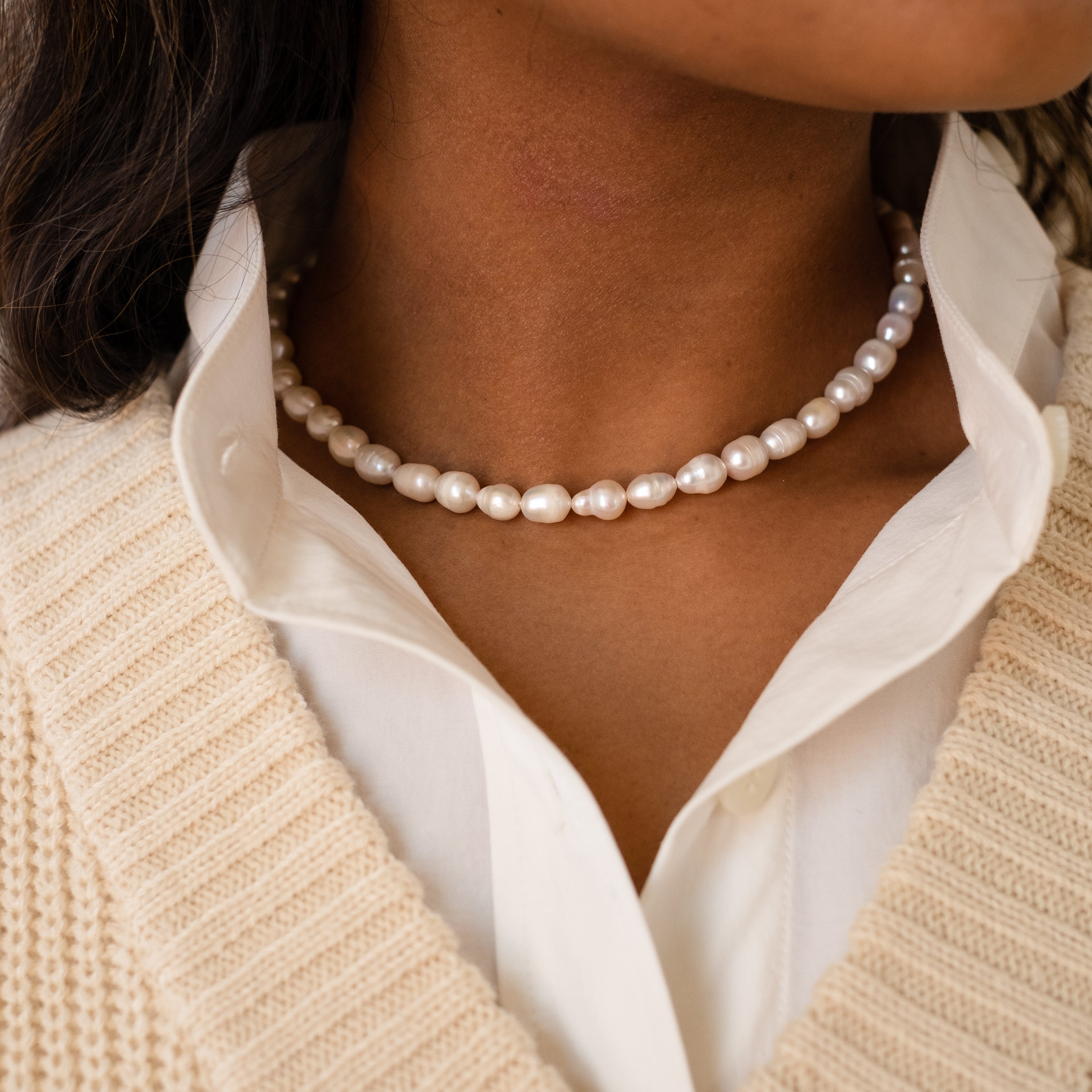 Chunky white freshwater pearls strung closely as a choker necklace, styled with a crisp white shirt and cream knit sweater layered over top.