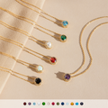 Gold necklaces with round gemstone pendants in assorted colors, each surrounded by a halo of small diamonds, including pearl, opal, emerald, amethyst, aquamarine, onyx and garnet, displayed on a neutral background.

