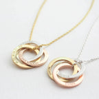 Two necklaces with interlocking circles in gold, silver, and rose gold, engraved with names, dates, and coordinates.