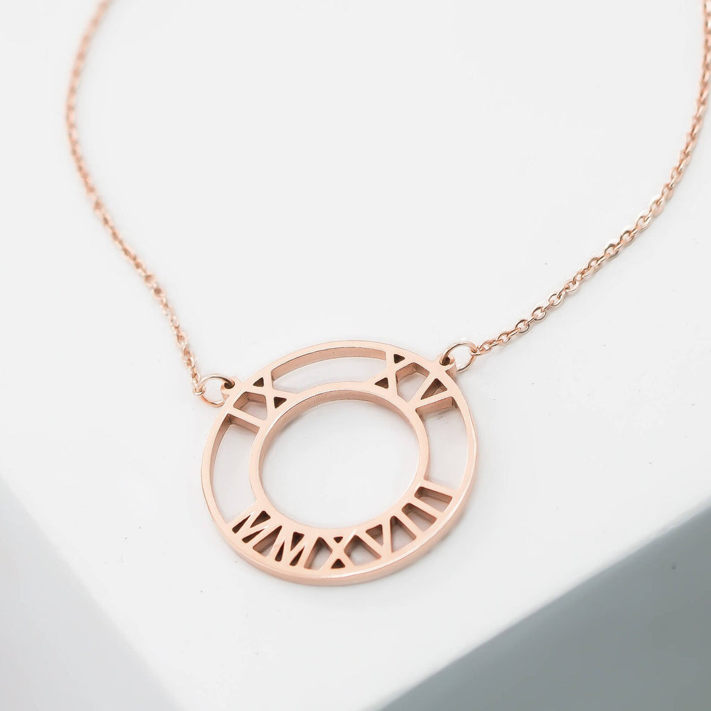 The Roman Numerals Necklace features a rose gold circular pendant with numerals cut out along the edge—a timeless milestone jewelry piece.