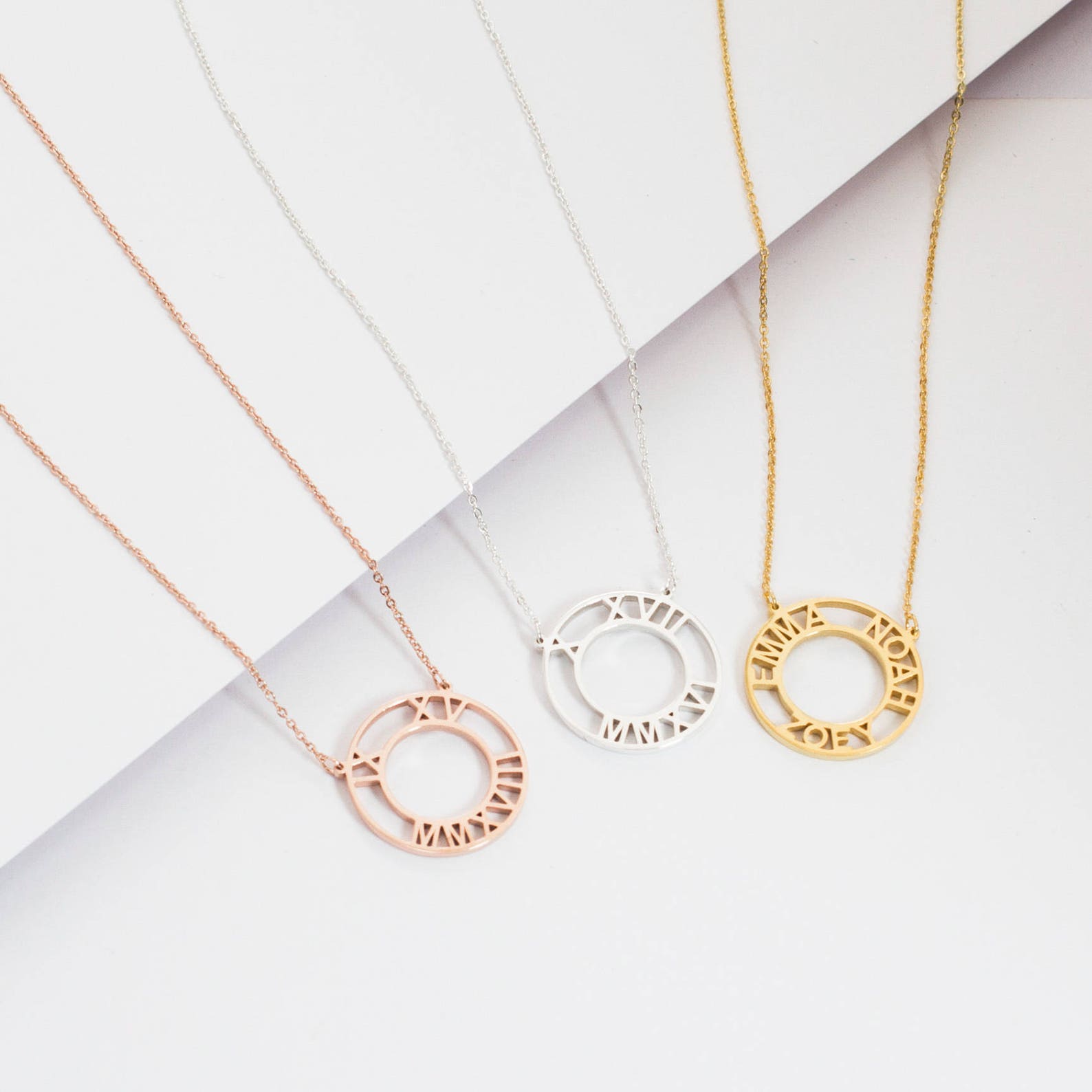 Three Roman Numerals Necklaces in rose gold, silver, and gold are displayed on a white background.